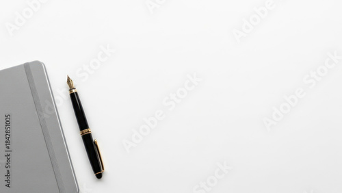 Minimalist flat lay image of a fountain pen and a grey notebook on a white background