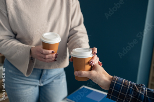 Tablou pe pânză Person offering takeaway coffee cup to colleague
