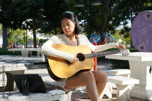 Young woman relaxing in park to do recreational activities, such as playing acoustic guitar in a park.