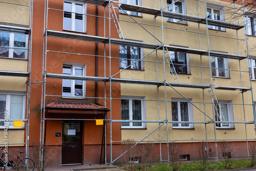 Renovation of the facade of a three-story apartment building. Steel scaffolding is set up against the building's wall.