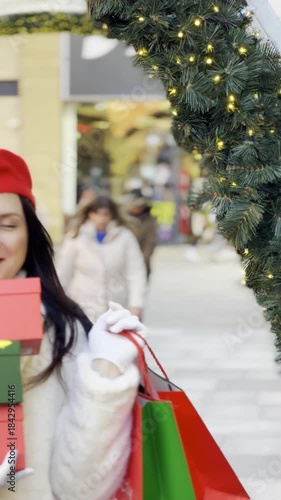 Girl in red beret holding gifts and bags walking along decorated holiday street