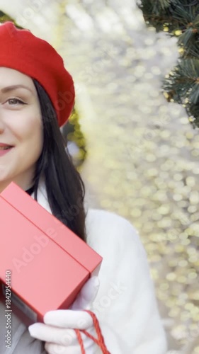 Girl in red beret holding gifts and bags walking along decorated holiday street