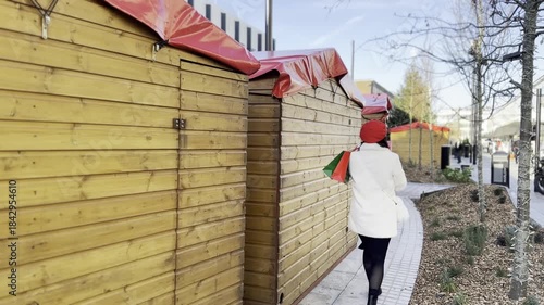 Girl in red beret holding gifts and bags walking along decorated holiday street