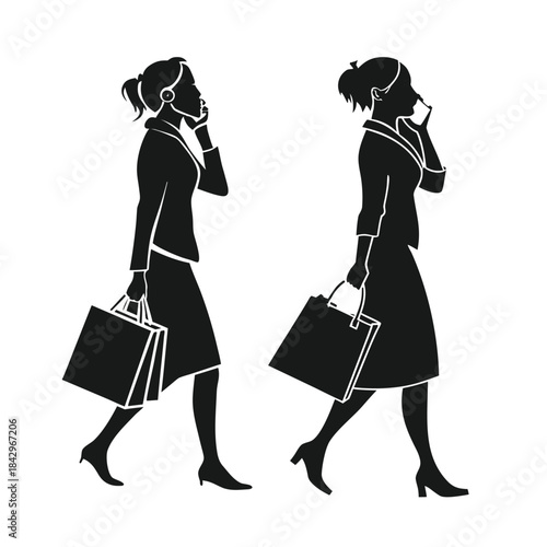 Silhouette of two businesswomen walking and talking on mobile phones while carrying shopping bags