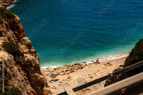 Fototapeta Naklejka Na Ścianę i Meble -  A secluded sandy beach with turquoise water nestled among rocks, featuring a person sitting in peaceful solitude. A perfect escape on the Mediterranean coast. Demre, Turkey.

