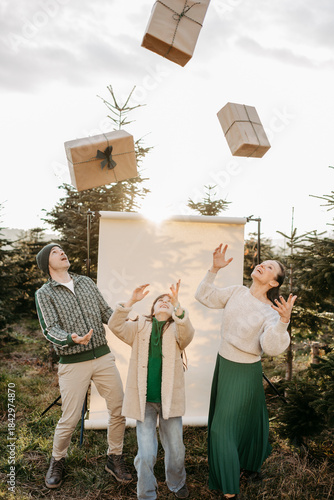 Familie steht in der Natur vor einem beigen Studiohintergrund und wirft Geschenke in die Luft