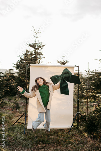 Mädchen mit grüner Masche in der Hand steht vor beigem Studiohintergrund in der Natur