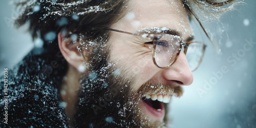 Joyful bearded man with glasses covered in snow smiling outdoors during a winter snowfall