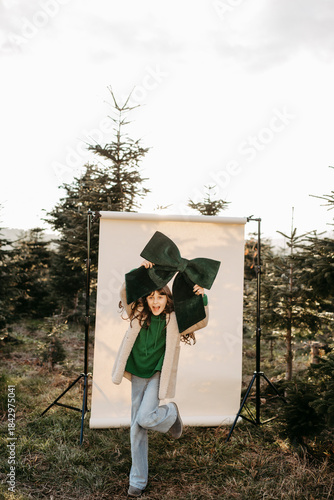 Mädchen mit grüner Masche in der Hand steht vor beigem Studiohintergrund in der Natur