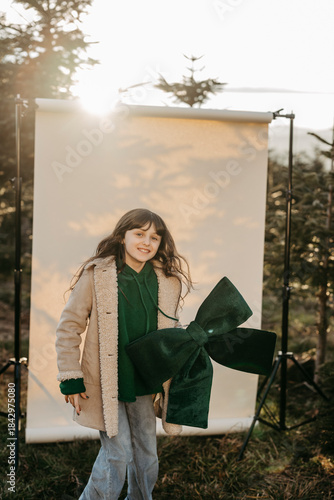 Mädchen mit grüner Masche in der Hand steht vor beigem Studiohintergrund in der Natur