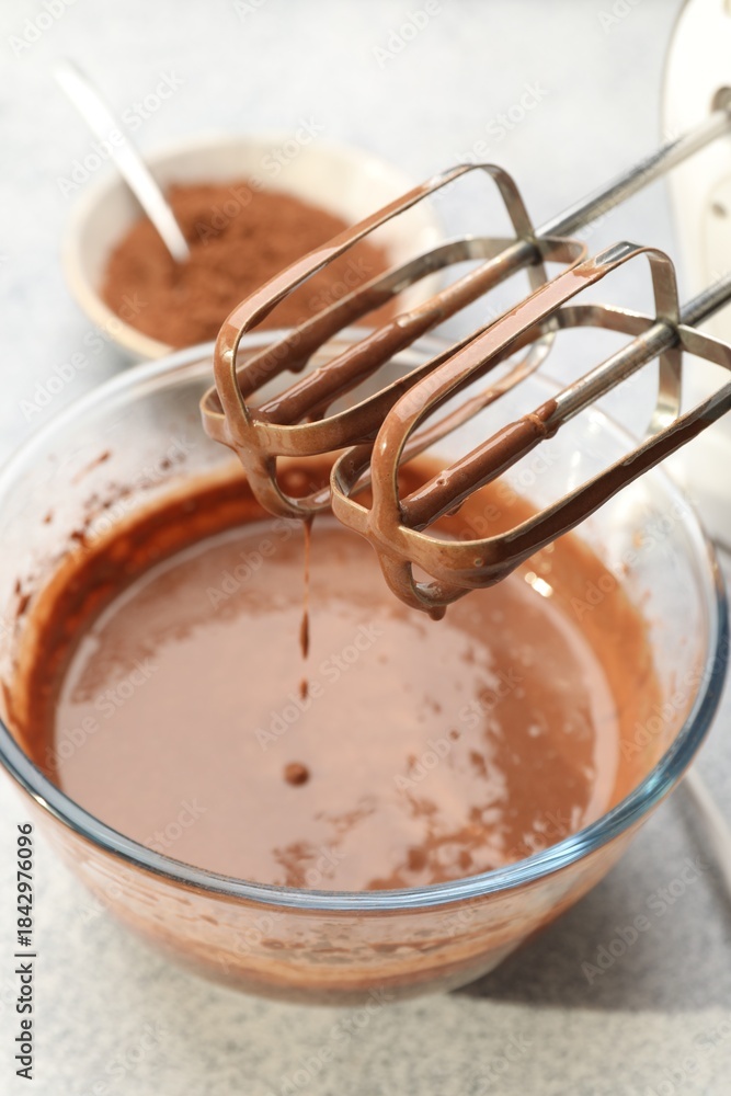 Fototapeta premium Dripping chocolate dough from mixer into bowl at grey textured table, closeup