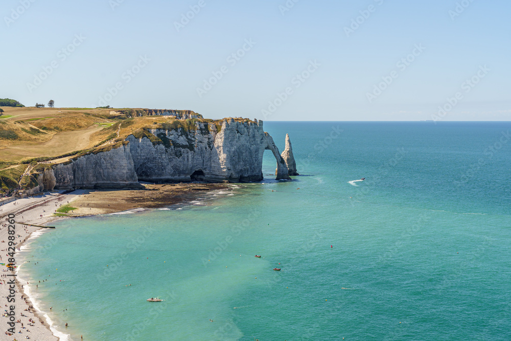Fototapeta premium Sarkozy Beach and Rocky Coast, made of stone, extending into the blue water of the ocean in the city of Etretat France The sky is blue The stone arch resembles an elephant's nose