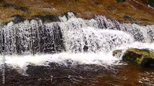 Water cascades over rocks in a river, creating splashes and ripples as it moves. slow motion