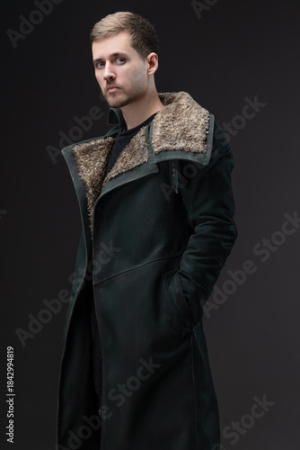 Melancholic cyberpunk style: man in oversized collar coat posing on studio gray.