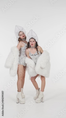 Two elegant women in sparkling snow queen costumes perform graceful poses and movements on white background. Festive winter video content for Christmas, New Year, fashion shows and seasonal marketing
