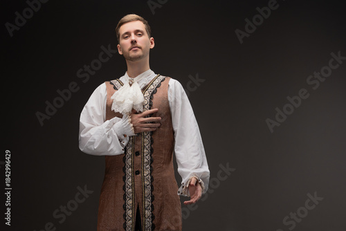 A young man in a theatrical costume in the style of Shakespeare's plays, photo on a gray background. Historical costume, Renaissance or Baroque character