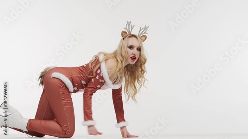 Woman in Christmas reindeer costume crawling into frame on white background. Playful holiday video content for Christmas, New Year storytelling, entertainment and seasonal marketing
