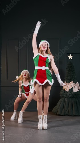 Three cheerful women in sexy elf costumes perform an energetic holiday dance in a dark studio with Christmas tree. Festive video concept for Christmas, New Year promotions, events seasonal marketing
