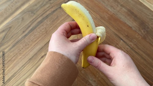 Female hand holding and peeling a banana on a wooden table. 