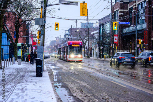 Red Toronto streetcar at an intersection on Queen St East in the Beaches neighbourhood on a slushy December morning, surrounded by fresh snowfall, wet roads, passing traffic and traffic lights
