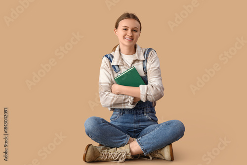 Young woman with book hugging herself on beige background