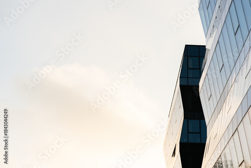 Contemporary glass office building with geometric lines and reflective windows, set against a bright sky. Suitable for business, architecture, and urban design concepts.