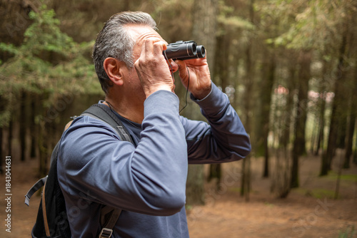Senior man birdwatching in a forest, enjoying nature during retirement