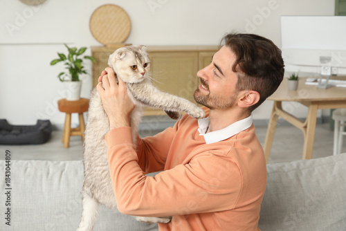 Young man holding cute Scottish fold cat at home