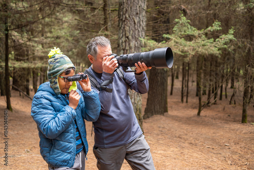 Grandfather and grandson enjoying nature, birdwatching, and photography hobby in forest