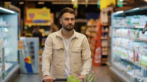 Handsome man pushing shopping cart in supermarket aisle