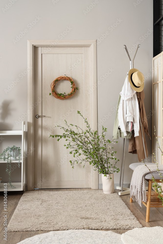 Fototapeta premium Door, clothes rack and vase with blossoming branches in stylish hall