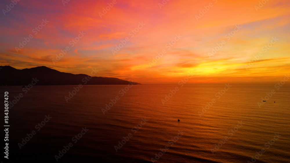 Naklejka premium Warm sunset illuminating da nang coastline, golden light painting tranquil waters with mountain silhouettes against dramatic vietnamese seascape