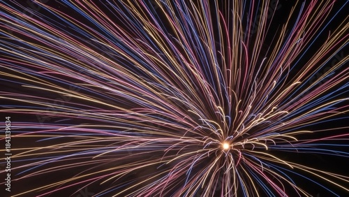 A vibrant burst of colorful fireworks explodes against a dark night sky, creating a dazzling display of light and motion.