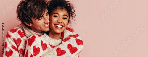 Young couple smiling while embracing in heart-patterned matching sweaters on pink background. Valentine's Day banner