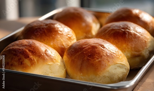 Some freshly baked hamburger buns, empty, still in a baking tray, shiny and golden from brushed melted butter, soft texture,