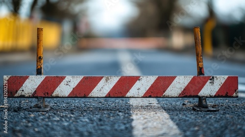 A roadblock with red and white stripes on a road with a blurred background.