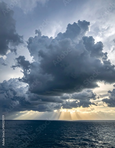 Dramatic view of ocean, dark clouds, and sun rays breaking through