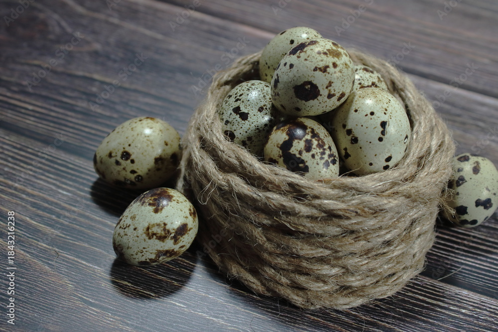 Obraz premium Fresh quail eggs arranged in a coiled jute rope nest on a dark wooden surface