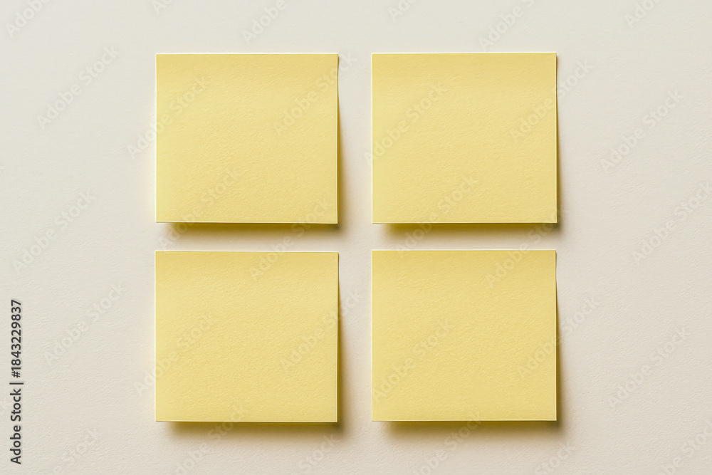 Fototapeta premium Horizontal photo of four yellow sticky notes arranged in a clean grid on a neutral background, bright and organized mood with soft shadows, minimal composition and clear structure, ideal for planning 