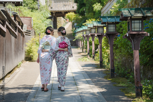 Fotografie Sisters or friends in yukata walking near wooden lanterns on approach to historic shrine