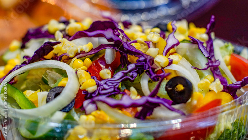 Close-up of fresh mixed vegetable salad with corn, red cabbage, onion, olives, lettuce and tomato in a clear plastic takeaway container. Healthy food, vegetarian meal, clean eating concept