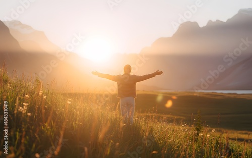Man standing in field with arms outstretched at sunrise