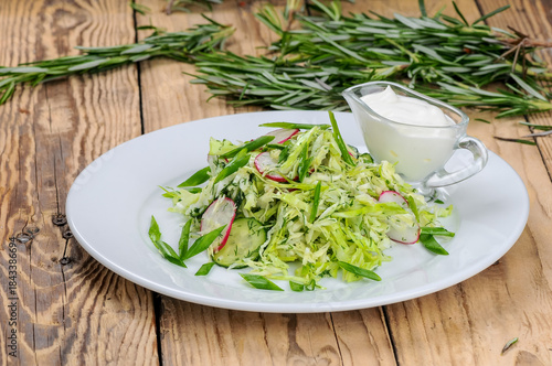 fresh cabbage and radish salad in a white plate on a wooden background with greens