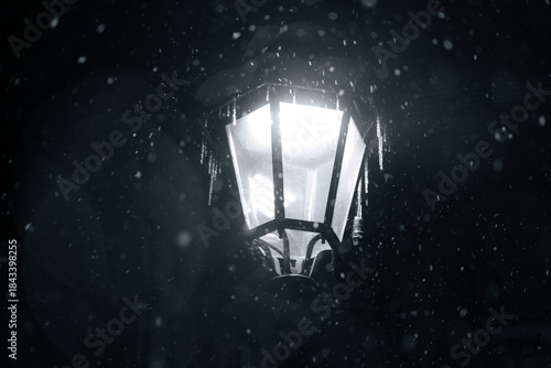 Fototapeta Naklejka Na Ścianę i Meble -  Bright lamp shines through falling snow in a dark winter evening outside a quiet street