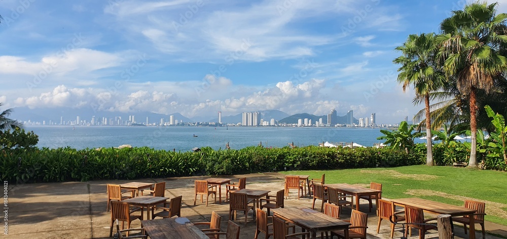 Outdoor restaurant terrace with wooden tables and chairs overlooking sea and city skyline, luxury tropical resort patio, summer vacation travel and hospitality concept