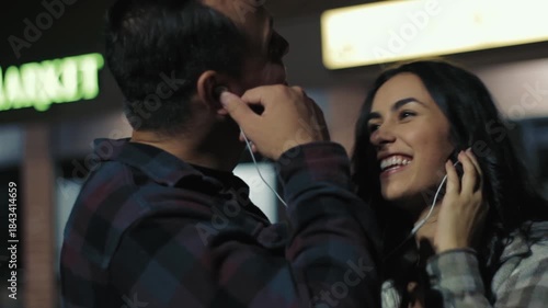 Wallpaper Mural Loving couple sharing headphones and laughing while listening to music at night Torontodigital.ca