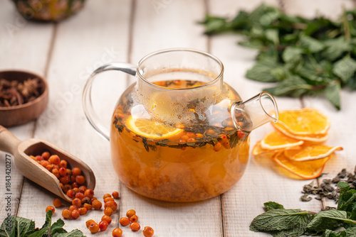 Aromatic sea buckthorn tea brewed with citrus slices herbs and spices served in a glass teapot on rustic table