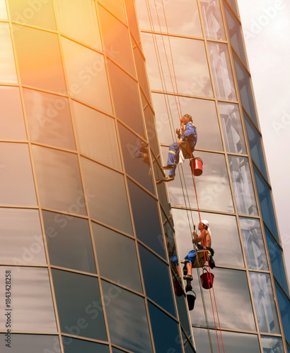 Workers are cleaning windows on a tall building in a busy urban area during sunlight hours