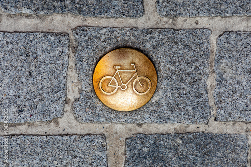 Golden bicycle icon plaque embedded in cobblestone pavement for urban transit theme