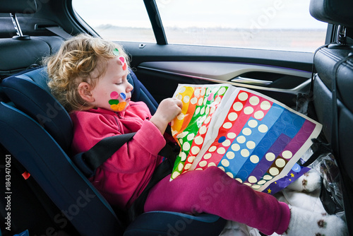 Belarus, Misk, 03.01.2024 Little girl in car safety seat playing with colorful stickers in vehicle. Child entertainment during long road trip.